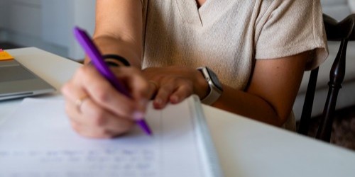 A person writing with a purple pen in a notebook