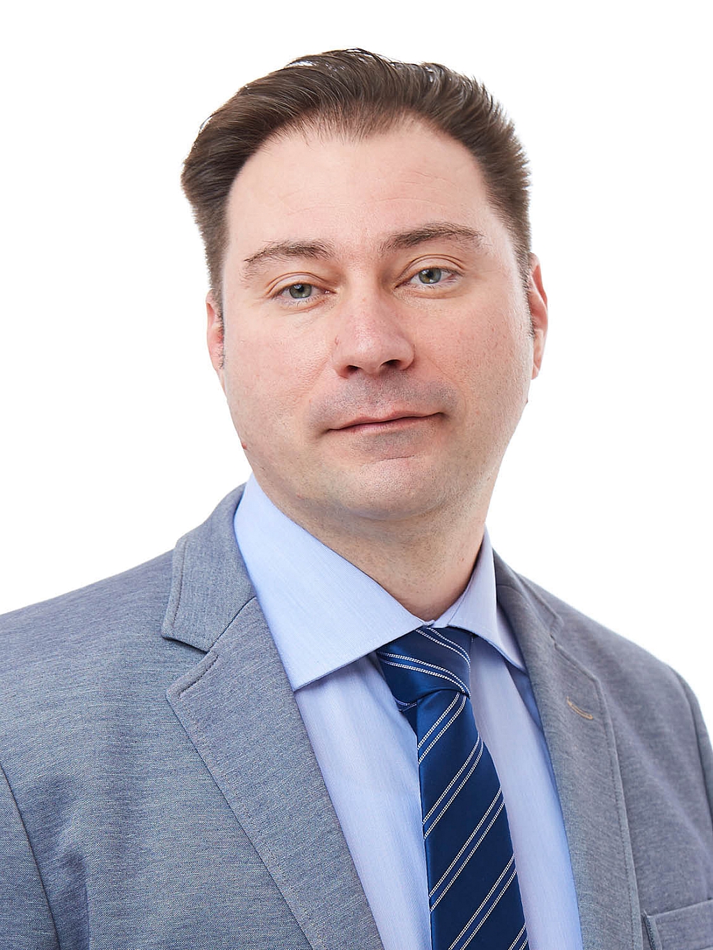 Man in a light blue dress shirt, blue striped tie, and grey suit jacket, facing forward with a neutral expression against a white background