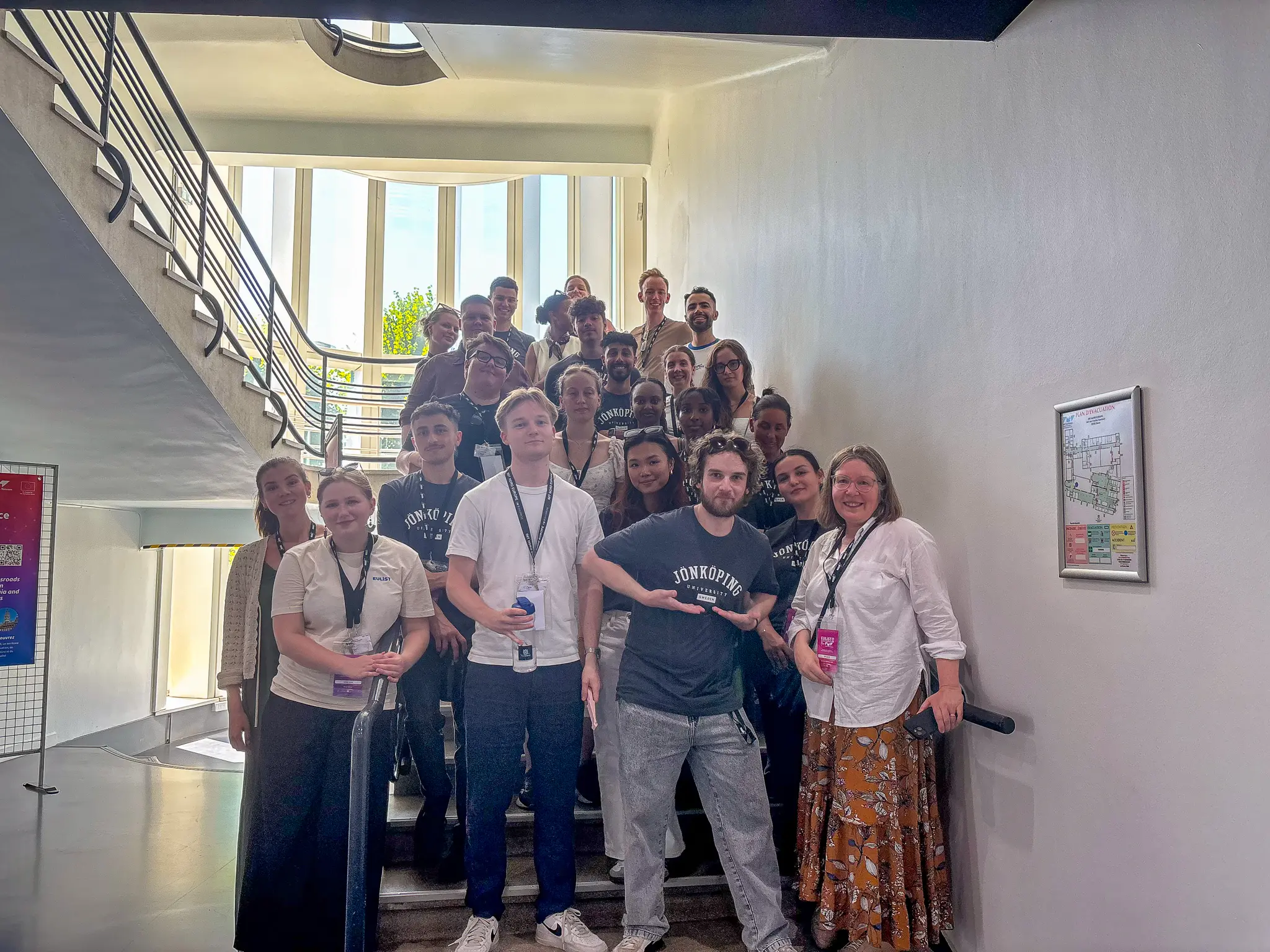 Ett 20-tal personer ler och kollar in i kameran när de står i en trappuppgång