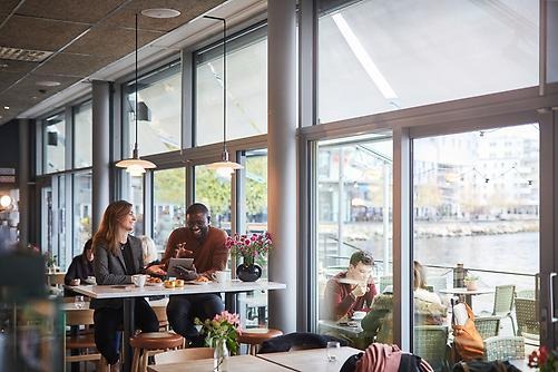 Couple in sit at a table by the window in a cafe in central Jönköping. Behind them is a view of Lake Munksjön.